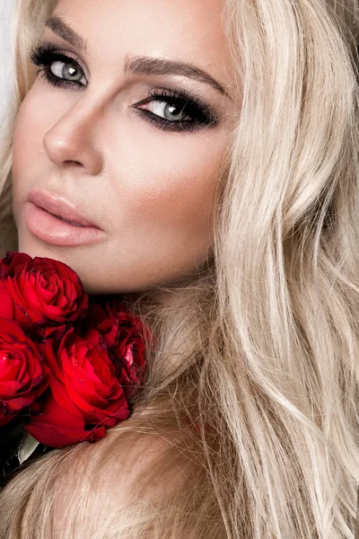 아름 다운 흰색 배경에 우아한 란제리에 섹시 한 금발. 빨간 장미 꽃다발을 들고 소녀. — 스톡 사진