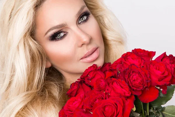 Güzel seksi sarışın beyaz bir arka plan üzerinde zarif iç çamaşırı. Bir buket kırmızı gül tutan kız.