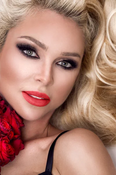 Güzel seksi sarışın beyaz bir arka plan üzerinde zarif iç çamaşırı. Bir buket kırmızı gül tutan kız.