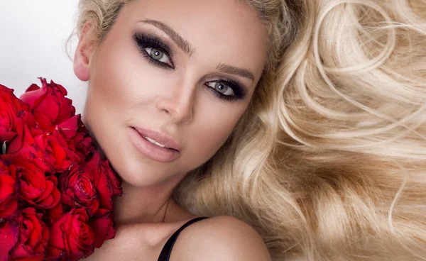 Güzel seksi sarışın beyaz bir arka plan üzerinde zarif iç çamaşırı. Bir buket kırmızı gül tutan kız.