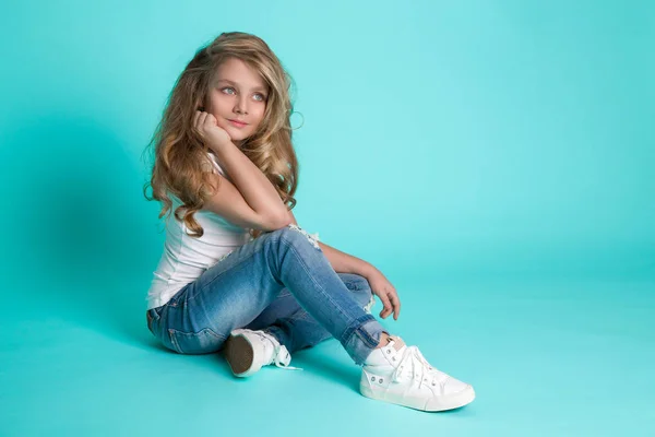 아름 다운 멋진 데님 청바지 파란색 배경에 자에 앉아 작은 금발 소녀 — 스톡 사진