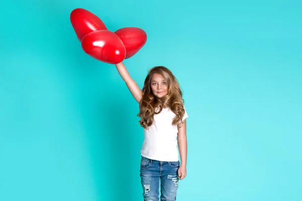 Beautiful stunning little blonde girl in denim jeans sitting on a chair on a blue background — Stock Photo, Image