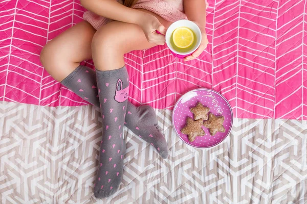 Sevimli küçük kız yatakta oturuyor ve çay içme anten ile sıcak bir kazak giyiyor