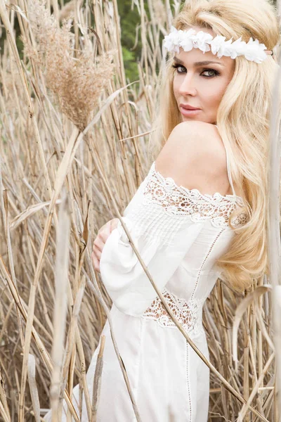 Stunning blonde sexy natural woman swing on a swing on a tree wearing a spring dress holding a bouquet of spring