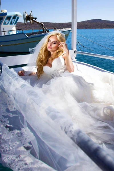 Hermosa novia rubia modelo femenino en vestido de novia increíble posa en la isla de Santorini en Grecia y más allá de ella es una hermosa vista — Foto de Stock