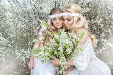 Güzel genç anne kızı bahar kıyafetleri ve bir çayır kürsüye çiçek çelenk giymiş ve snuggling ile