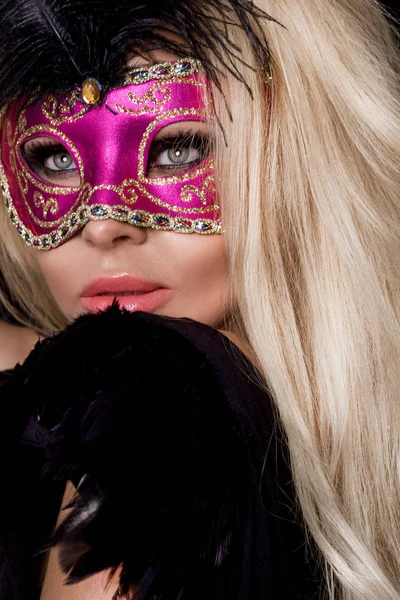 Mooie blonde sensuele vrouw met carnaval masker, staande op een achtergrond van zwarte ballonnen en sexy in de lens kijkt — Stockfoto