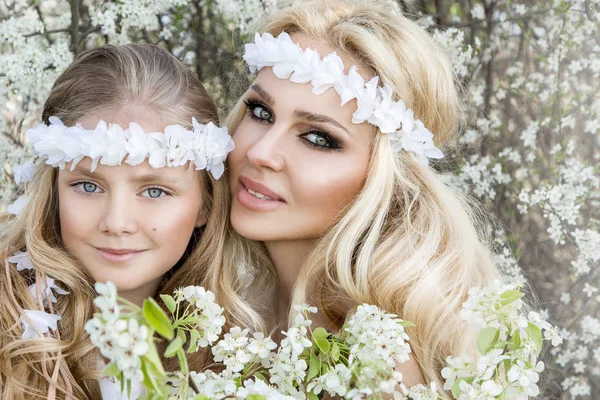 Bela jovem mãe com sua filha vestida com roupas de primavera e grinaldas de flores em um prado e aconchegante — Fotografia de Stock