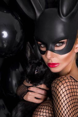 Güzel seksi sarışın kadın karnaval maskesi, siyah balon ve seksi bir arka plan üzerinde duran lense benziyor.