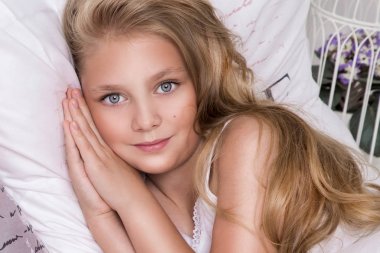 Nazik genç güzel sarışın kız, uzun saçlı ve mavi gözlü, küçük Prenses çocuk yatakta, keten kelebekler ve sevinçle gülümsüyor, uyuyan yatıyor