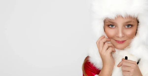 Fantastisk vacker liten flicka med lång blond, klädd i en röd mössa Santa Claus och eleganta kläder står på en vit bakgrund och titta glatt in i linsen — Stockfoto