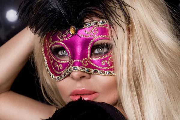 Mooie blonde sensuele vrouw met carnaval masker, staande op een achtergrond van zwarte ballonnen en sexy in de lens kijkt — Stockfoto