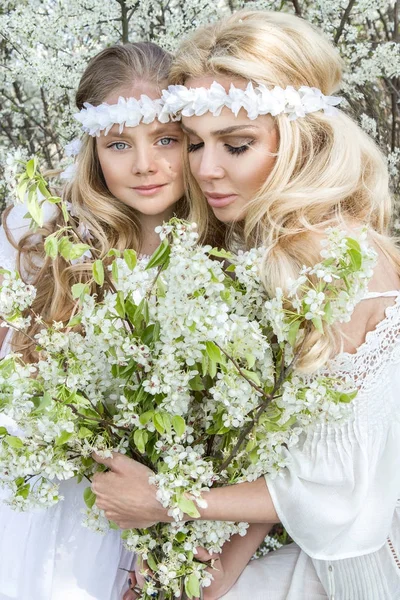 Güzel genç anne kızı bahar kıyafetleri ve bir çayır kürsüye çiçek çelenk giymiş ve snuggling ile