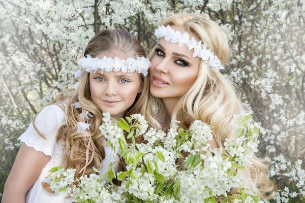 Bela jovem mãe com sua filha vestida com roupas de primavera e grinaldas de flores em um prado e aconchegante — Fotografia de Stock