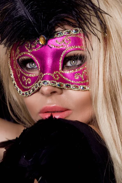 Mooie blonde sensuele vrouw met carnaval masker, staande op een achtergrond van zwarte ballonnen en sexy in de lens kijkt — Stockfoto