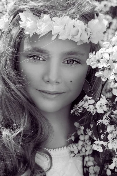 Menina bonito com longos cabelos loiros em pé em um prado em grinalda de flores, segurando um buquê de flores da primavera e vestido com roupas de primavera — Fotografia de Stock