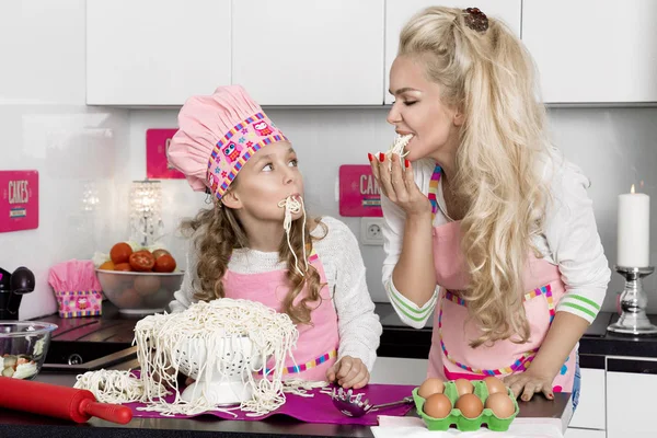 Vackra fantastisk kvinna mor och dotter i förkläden kök matlagning i köket cookies och nudlar pasta — Stockfoto