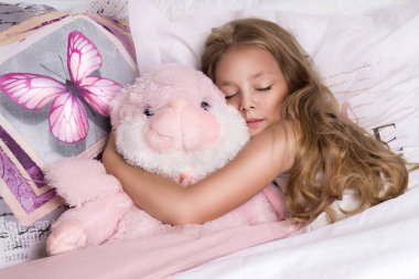 Nazik genç güzel sarışın kız, uzun saçlı ve mavi gözlü, küçük Prenses çocuk yatakta, keten kelebekler ve sevinçle gülümsüyor, uyuyan yatıyor