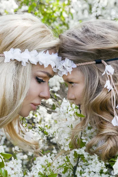 Bela jovem mãe com sua filha vestida com roupas de primavera e grinaldas de flores em um prado e aconchegante — Fotografia de Stock