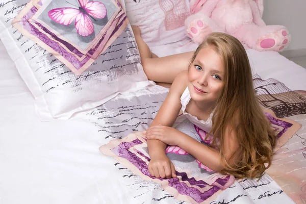 Gracious young beautiful blond girl, little princess with long hair and blue eyes, the child lies in bed, sleeping in linen in butterflies and joyfully smiles — Stock Photo, Image