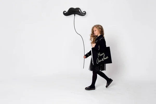 Милосердная элегантно одетая маленькая девочка идет по магазинам с сумкой на плече и рукой, держащей воздушный шар — стоковое фото