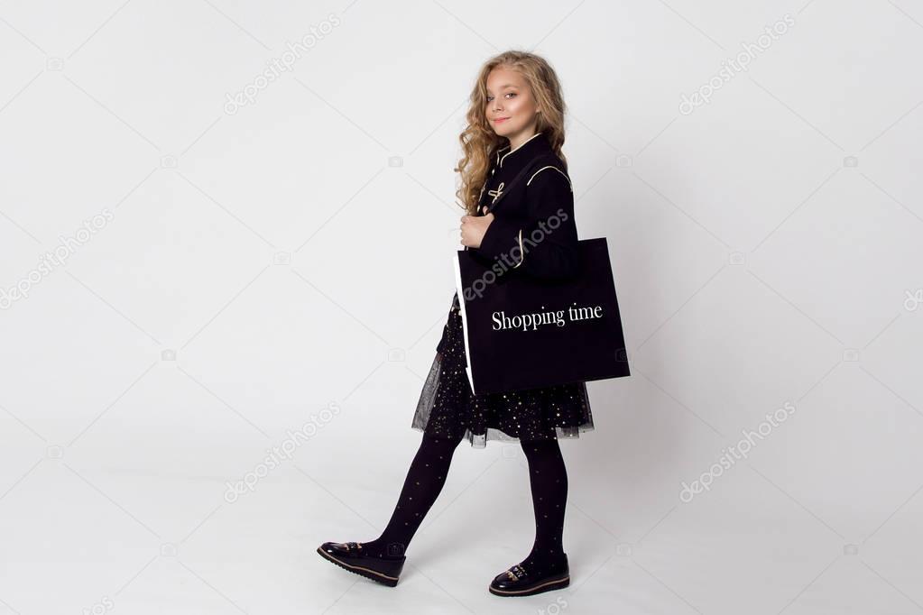 Gracious elegantly dressed little girl goes shopping with a bag on his shoulder