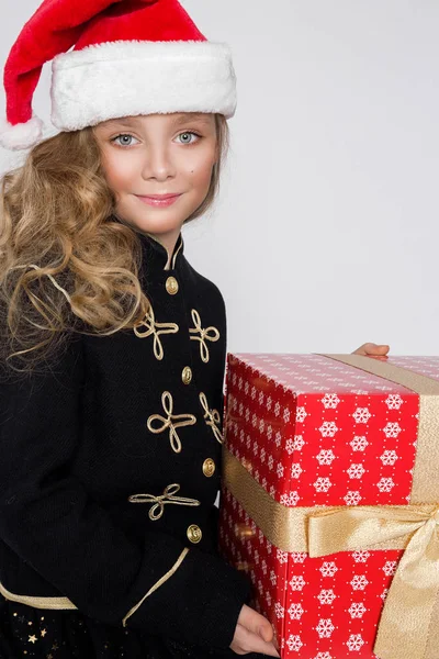 Splendida bella bambina con lunghi capelli biondi tiene tra le mani i regali, guarda gioiosamente nella lente nel periodo natalizio — Foto Stock