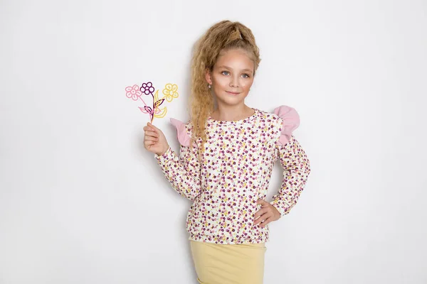 Ohromující krásná holčička s dlouhé blond vlasy stojící na bílém pozadí a drží balon a květiny v ruce — Stock fotografie