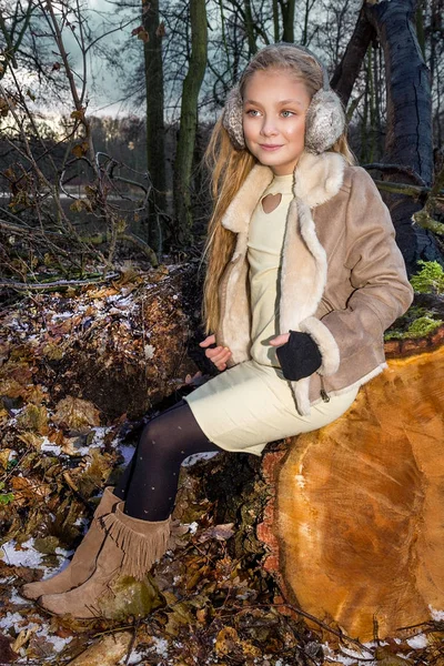 Hermosa niña dulce vestida con un abrigo de piel de oveja y botas sentadas en el tronco y en el fondo es la increíble vista del otoño y el invierno — Foto de Stock
