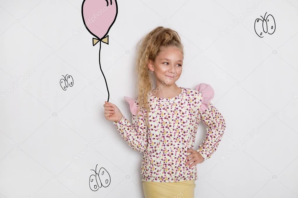 Stunning beautiful little girl with long blond hair standing on a white background and holds a balloon and flowers in his hand