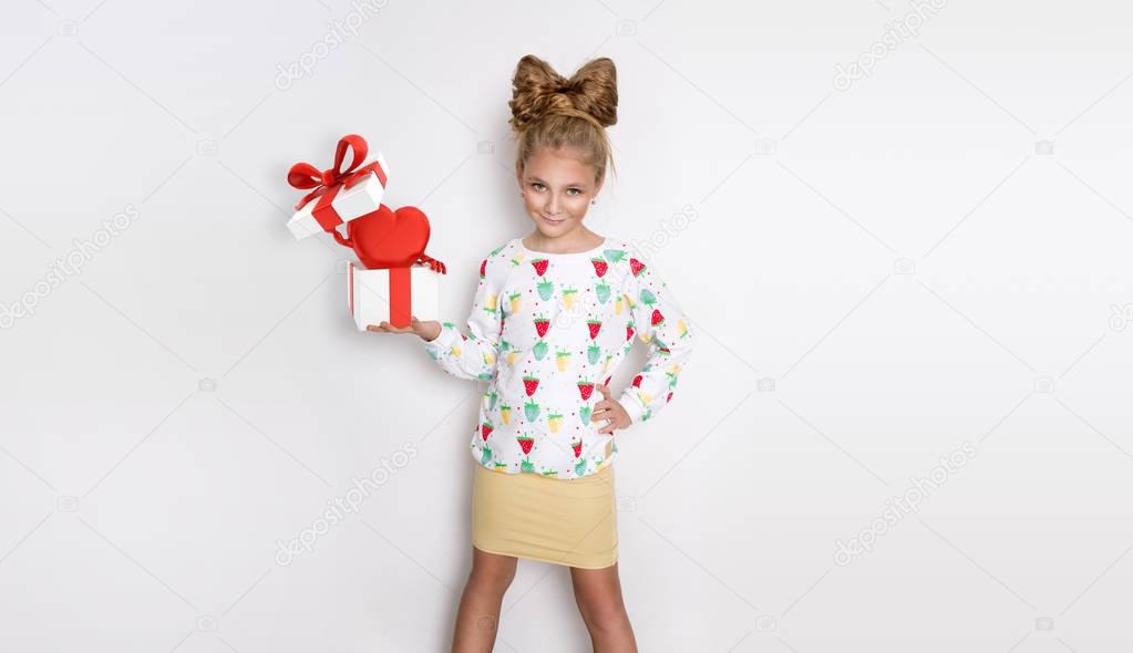 Gracious little girl with blond hair and blue eyes standing on a white background wearing a sweatshirt and a strawberry in his hand holding a bowl with fresh strawberries