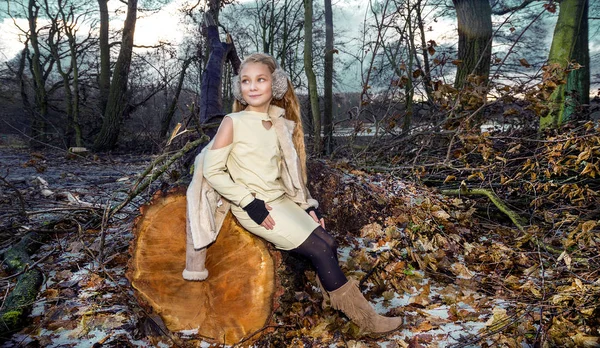 Mooie zoete meisje gekleed in een schapenvacht jas en laarzen zittend op de stam en op de achtergrond is de adembenemend uitzicht op de herfst en winter — Stockfoto
