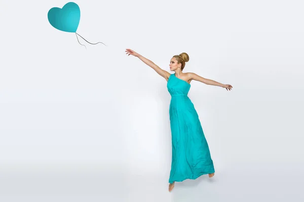 A beautiful woman in a long dress dances and catches a balloon — Stock Photo, Image