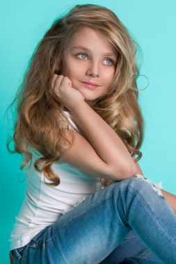 Güzel denim Jeans mavi bir arka plan bir sandalyede oturan küçük sarışın kız çarpıcı