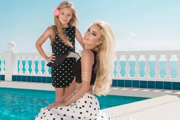 Güzel sarışın genç anne ve kızı, puantiyeli elbise giymiş. Santorini Adası denizin muhteşem görüntüsü üzerinde duruyorlar.