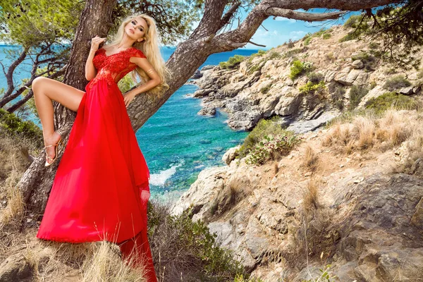 Сексуальна модель в довгій, червоній, вечірній сукні, що стоїть біля басейну і розкішного готелю і на задньому плані має дивовижний вид — стокове фото