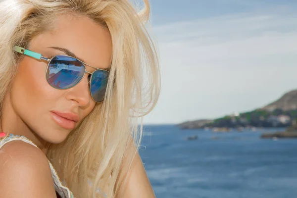 Piękne wspaniałe kobiety Blondynka w okularach słonecznych i eleganckie ubrania i bikini przy basenie ze wspaniałym widokiem na morze i wyspy Santorini — Zdjęcie stockowe