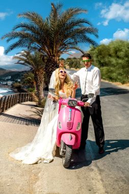 Güzel genç çift, sarışın kadın model scooter Santorini Yunanistan üzerinde oturan şaşırtıcı düğün giysileri içinde kocasıyla.