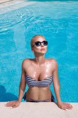 Bikini ve güneşli bir günde ve sensually muhteşem manzaralı havuzunda duran güneş gözlüğü mükemmel yüzüne olağanüstü çarpıcı zarif lüks seksi sarışın model güzel kadınla lense benziyor
