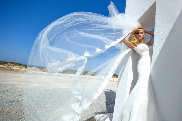 Hermosa novia rubia modelo femenino en vestido de novia increíble posa en la isla de Santorini en Grecia y más allá de ella es una hermosa vista — Foto de Stock