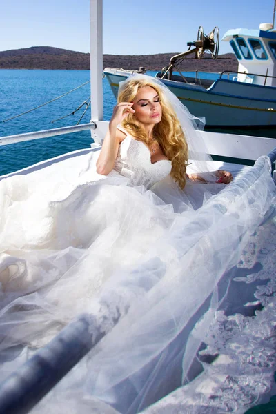 Hermosa novia rubia modelo femenino en vestido de novia increíble posa en la isla de Santorini en Grecia y más allá de ella es una hermosa vista — Foto de Stock