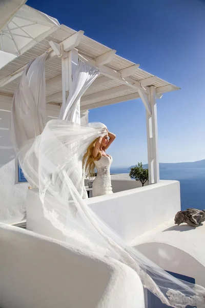 Hermosa novia rubia modelo femenino en vestido de novia increíble posa en la isla de Santorini en Grecia y más allá de ella es una hermosa vista —  Fotos de Stock