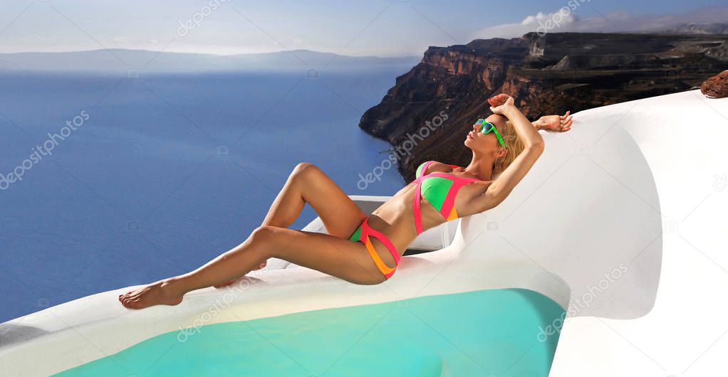 Beautiful bride blonde female model in amazing wedding dress poses on the island of Santorini in Greece and beyond it is a beautiful view