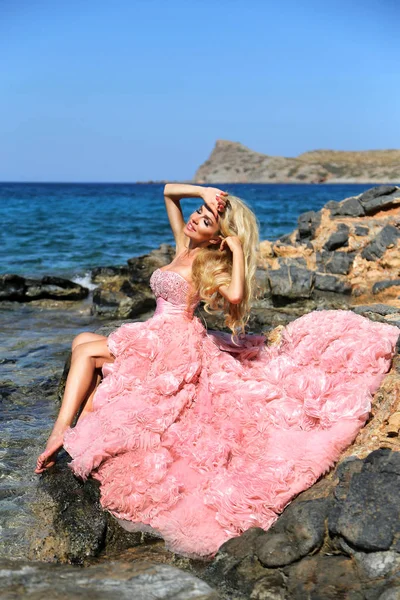 Beautiful bride blonde female model in amazing wedding dress poses on the island of Santorini in Greece and beyond it is a beautiful view — Stock Photo, Image