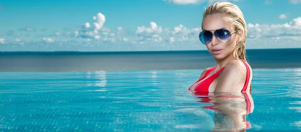 Modelo de mulher loira bonita com cabelo molhado e maquiagem elegante sentado em uma piscina com vistas incríveis em um hotel de luxo, vestindo jóias, brincos com os cristais e corpo nu molhado — Fotografia de Stock