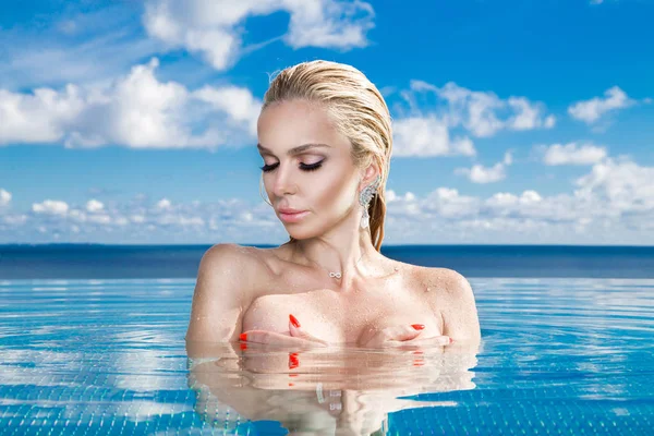 Vacker blond kvinna modell med blött hår och elegant makeup sitter i en pool med fantastisk utsikt i ett lyxhotell, bära smycken, örhängen med kristaller och våta nakna kropp — Stockfoto