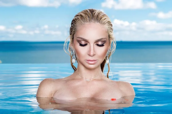 Islak saç ve zarif makyaj takı, kristal ve ıslak çıplak vücut ile küpeler harika manzaralı lüks otel, bir havuzda oturan güzel sarışın kadın model