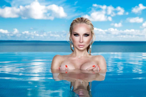 Islak saç ve zarif makyaj takı, kristal ve ıslak çıplak vücut ile küpeler harika manzaralı lüks otel, bir havuzda oturan güzel sarışın kadın model