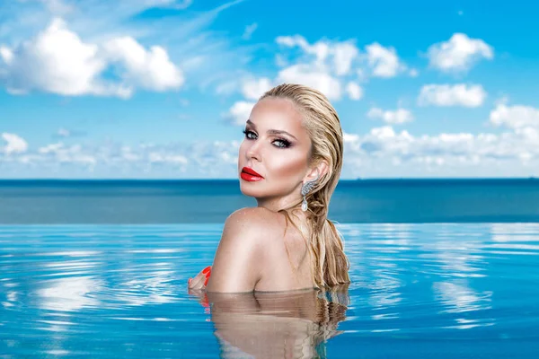 Islak saç ve zarif makyaj takı, kristal ve ıslak çıplak vücut ile küpeler harika manzaralı lüks otel, bir havuzda oturan güzel sarışın kadın model