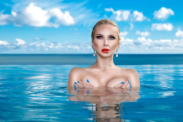 Modelo de mulher loira bonita com cabelo molhado e maquiagem elegante sentado em uma piscina com vistas incríveis em um hotel de luxo, vestindo jóias, brincos com os cristais e corpo nu molhado — Fotografia de Stock